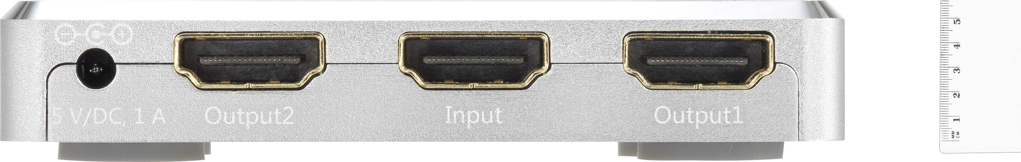 Een zilveren HDMI-splitter met drie HDMI-poorten: 'Output2', 'Input', 'Output1'. Links een DC-aansluiting, rechts een liniaal.