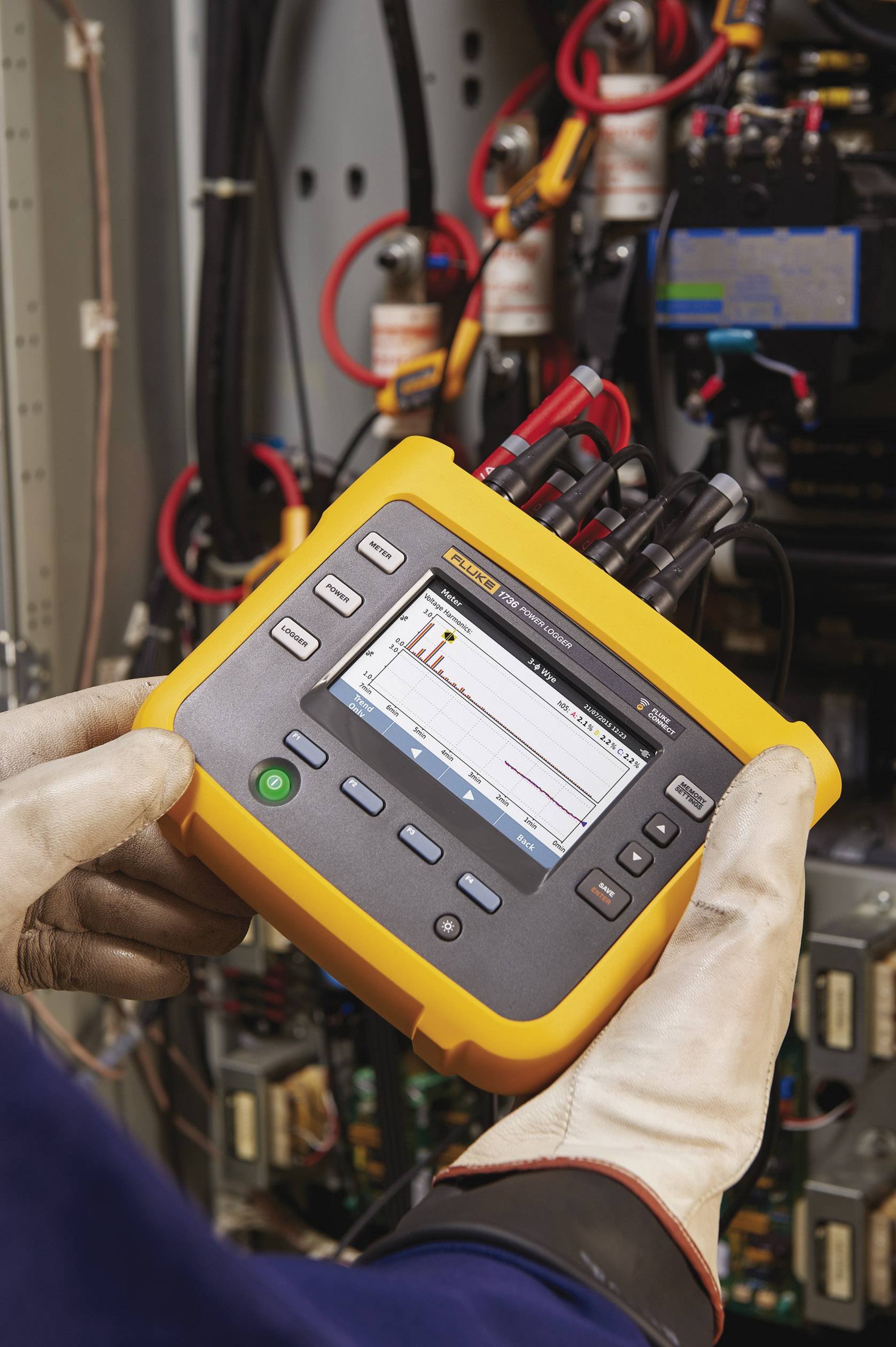 Een persoon houdt een handzaam meetapparaat met een scherm in de elektronische kast, waarop een grafische grafiek zichtbaar is.