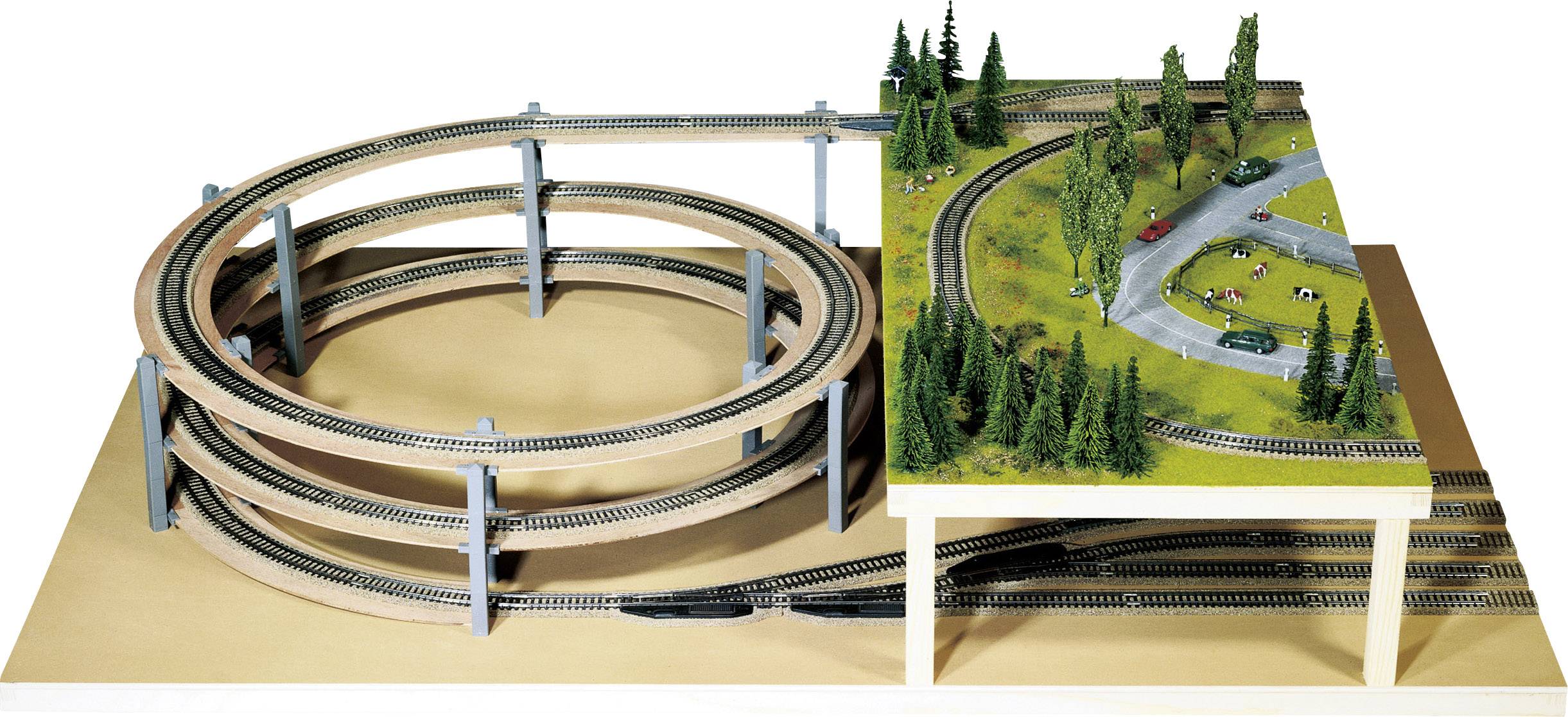 Modelspoorbaan met een dubbele, spiraalvormige houten helling links en een gedetailleerd landschap met bomen en auto's rechts.