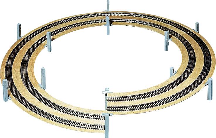 Modelspoorbaan kruising op een verhoogd houten frame met dubbele sporen, ondersteund door metalen palen, weergegeven in een cirkelvormige configuratie.