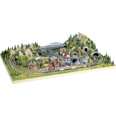 Modelbaan-landschap met treinen op sporen, bruggen, tunnels, gebouwen en bomen op heuvelachtig terrein.
