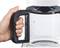 Een hand houdt de greep vast van een transparante koffiepot met maatschaal, aangesloten op een koffiezetapparaat.