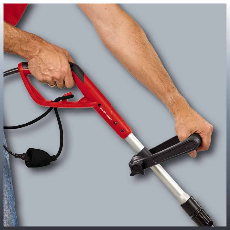 Een persoon houdt een rode hogedrukreiniger met een zwart snoer. De focus ligt op de manier van vasthouden van het apparaat.