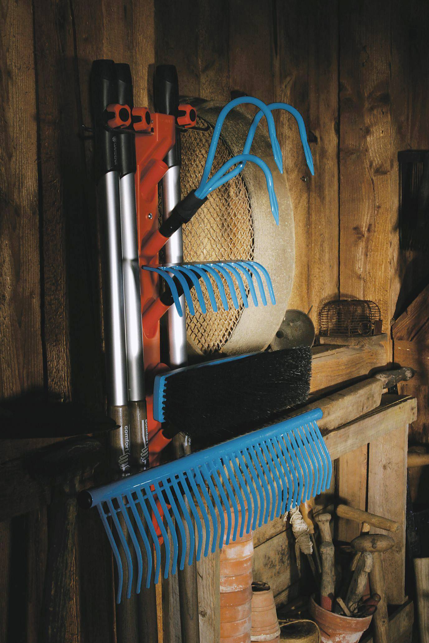 Wandhouder met tuingereedschappen zoals hark en bezem in een houten schuur. Gereedschappen zijn netjes opgehangen voor gemakkelijke bereikbaarheid.
