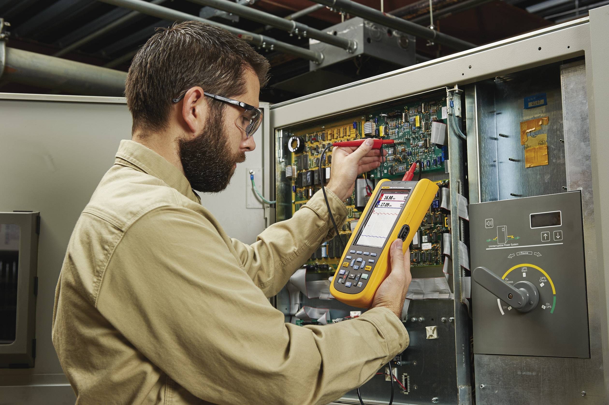 Een technicus met veiligheidsbril gebruikt een multimeter voor het onderhoud van een elektrisch schakelbord in een industriële omgeving.