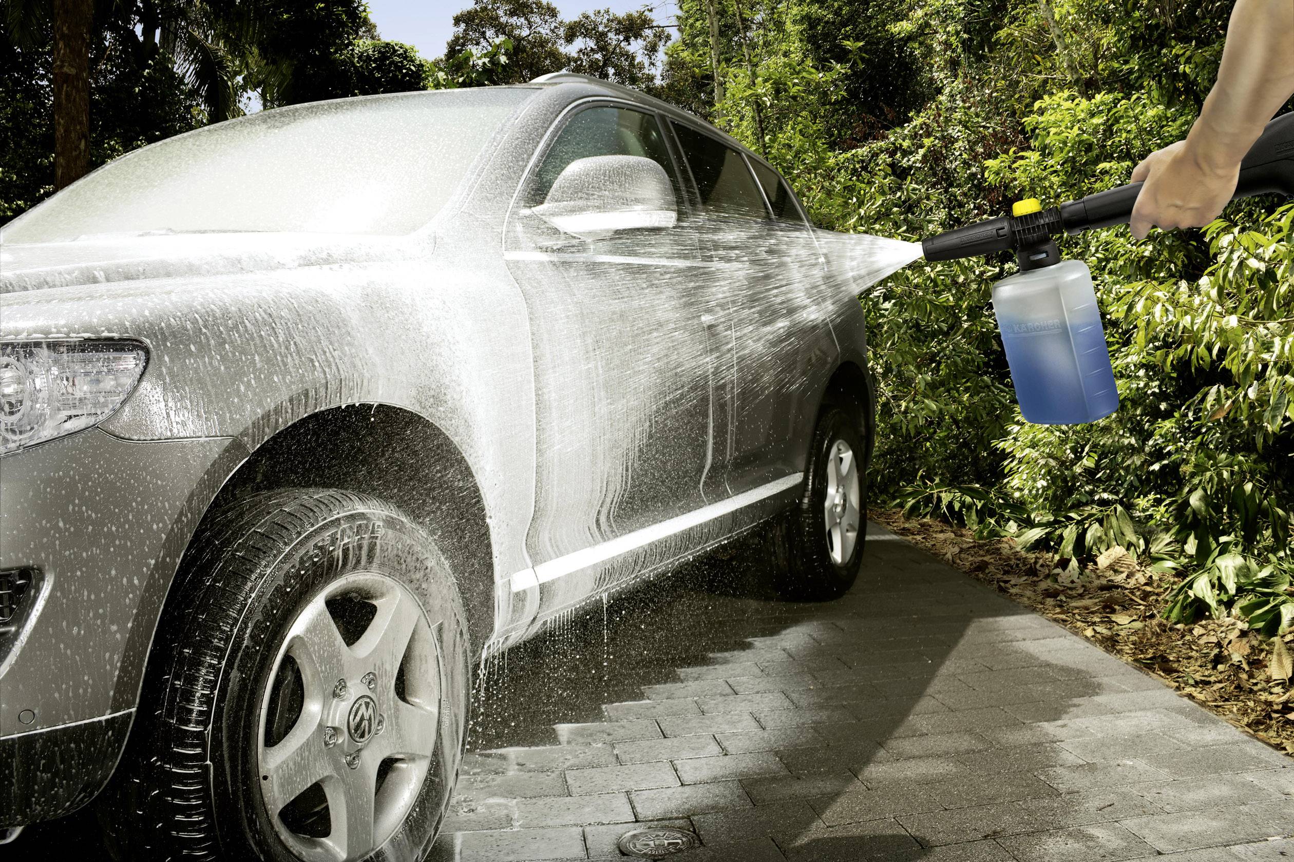 Een auto wordt buiten schoongemaakt met een hogedrukreiniger. Schuim bedekt het oppervlak, terwijl water in het zonlicht fonkelt.