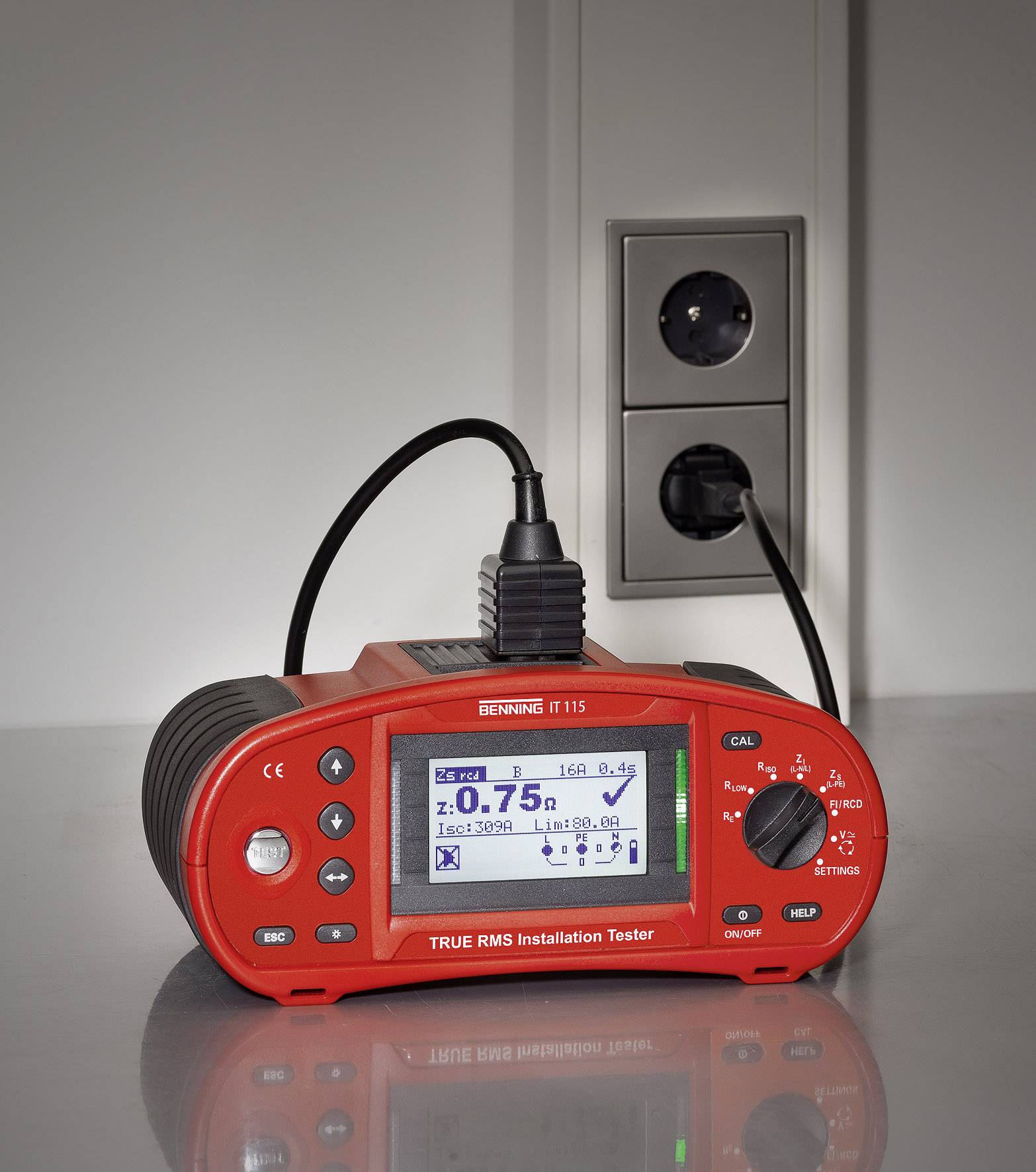 Een rood installatie-meetapparaat is aangesloten op een stopcontact en toont meetwaarden op het display.