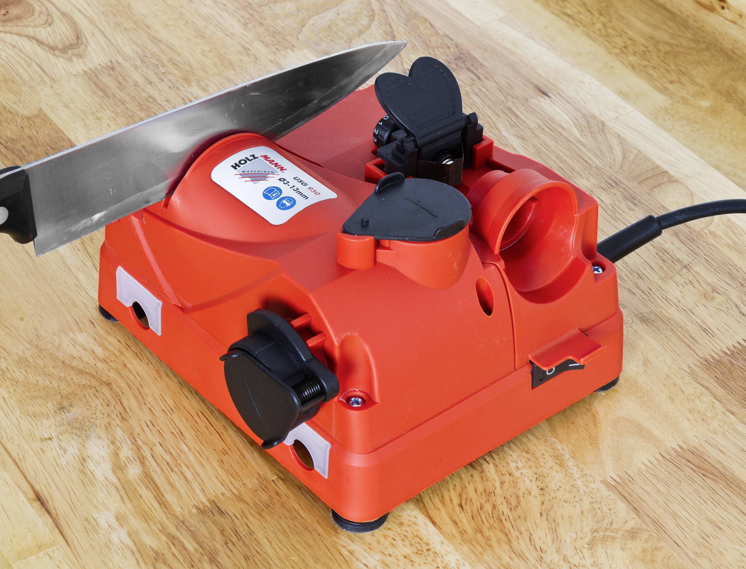 Elektrische messenslijper op een houten tafel. Een mes is bevestigd in de slijpinrichting. Het apparaat is rood en heeft een stroomkabel.