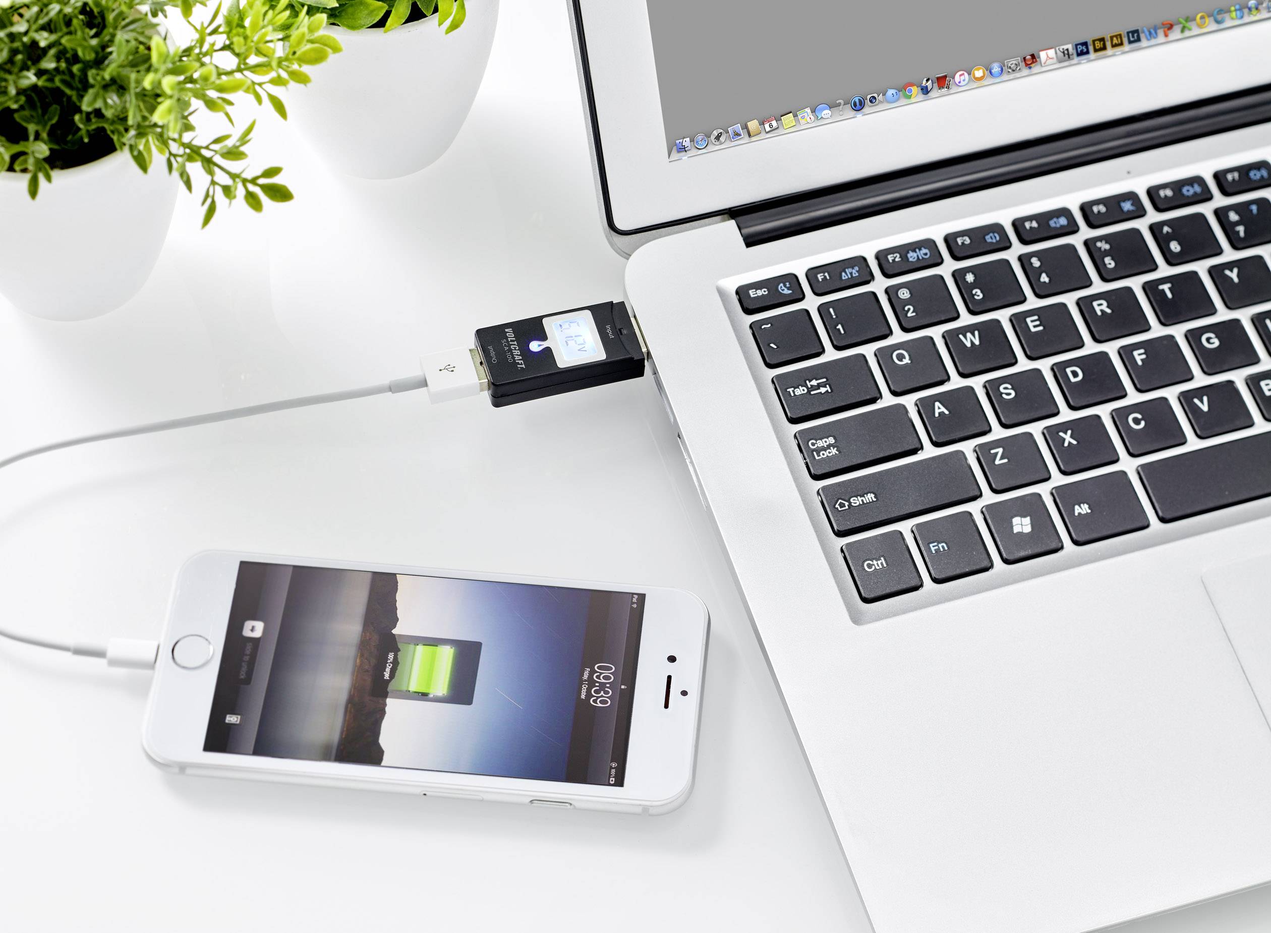 Een smartphone wordt via een USB-kabel verbonden met een laptop en opgeladen. Ernaast staat een plant op tafel.