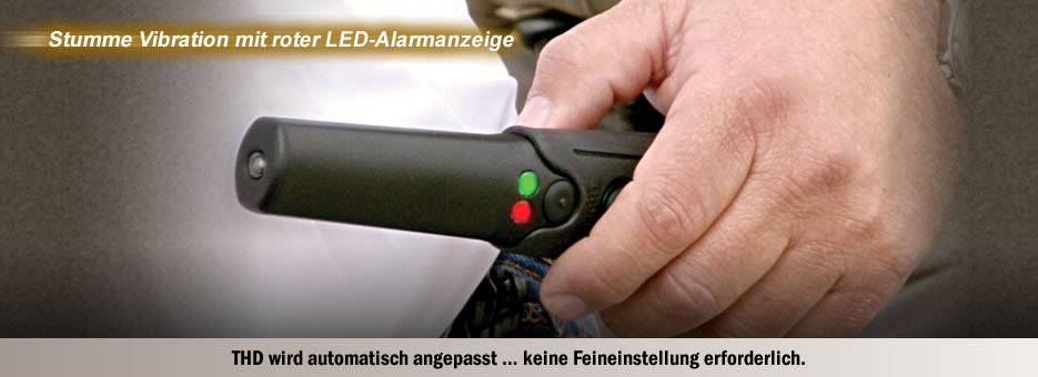 Hand houdt een zwarte vibratiedetector met rode en groene LED-lampjes. Tekst bovenaan: 'Stille trillingswaarschuwing met rode LED-alarmweergave.'
