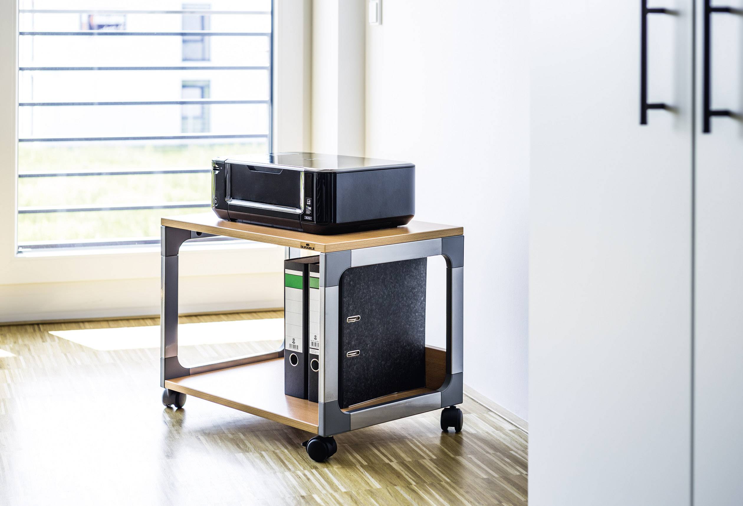 'Printer op een kleine, verrijdbare tafel met drie mappen eronder, in een lichte, moderne kantoorruimte met houten vloer.'