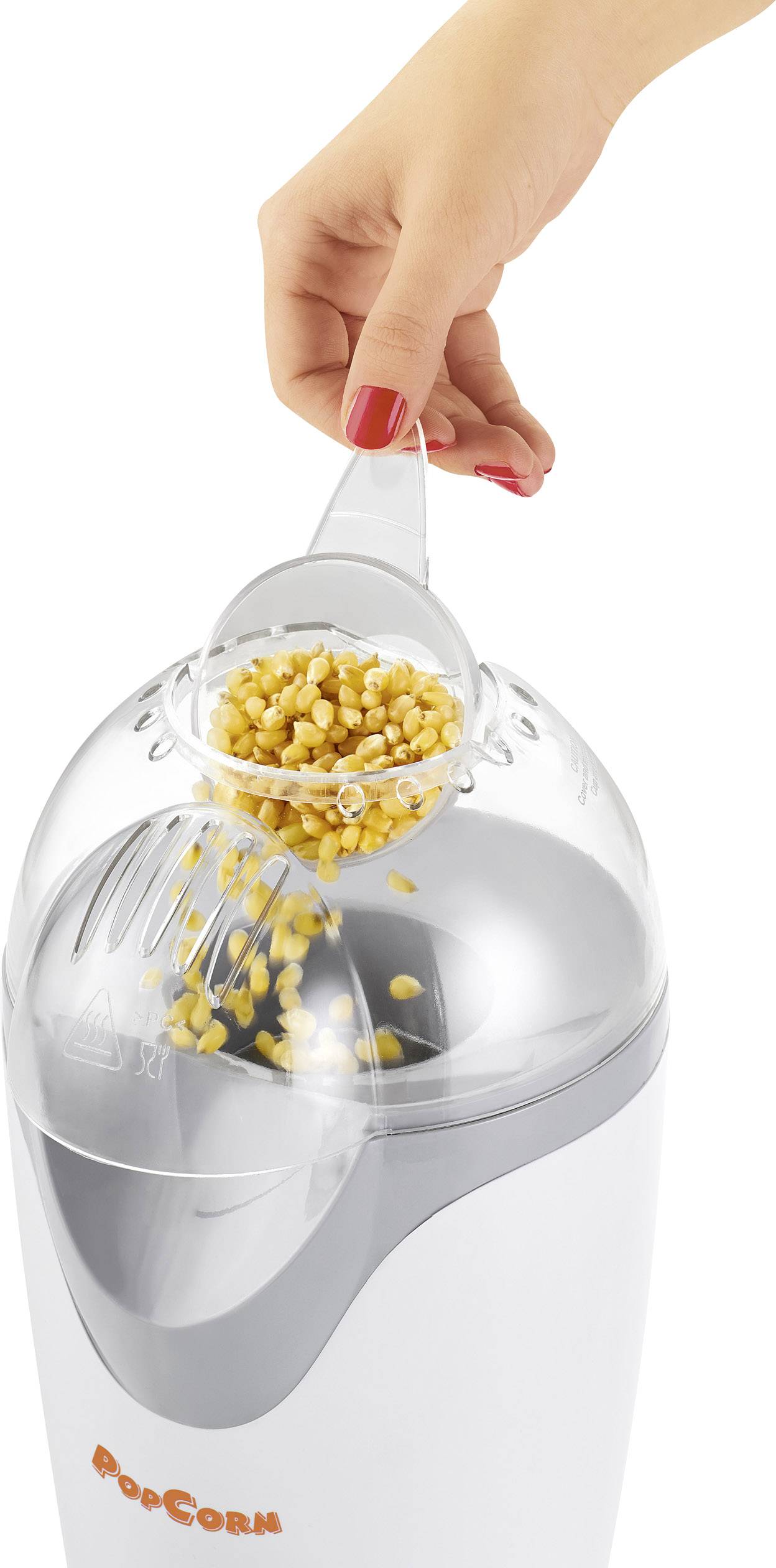 Een hand vult gele maiskorrels in een witte popcornmachine met een transparante deksel.