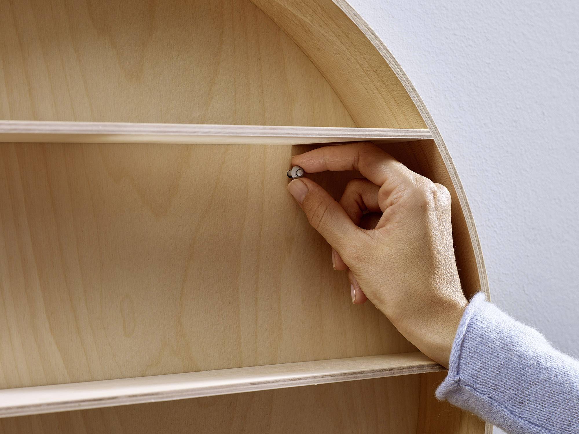 Een hand stelt een kleine metalen pen bij in een licht houten rek met meerdere vakken.