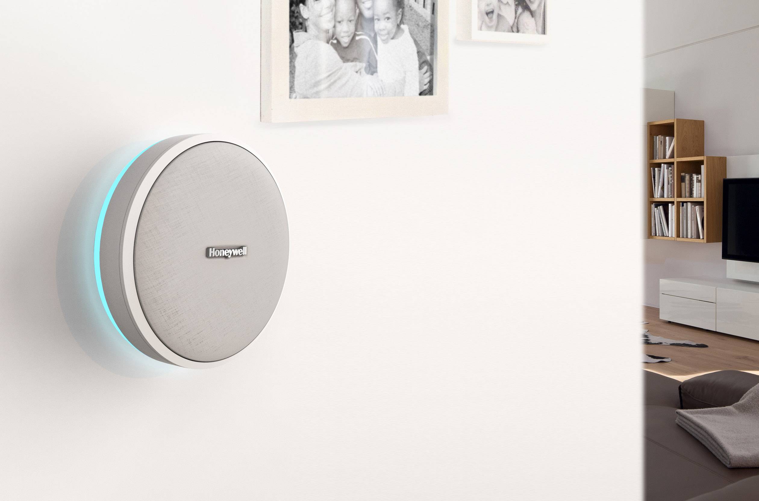 Slimme thermostaat aan de muur in een woonkamer, naast twee fotolijsten. Woonkamermeubilair en televisie op de achtergrond.