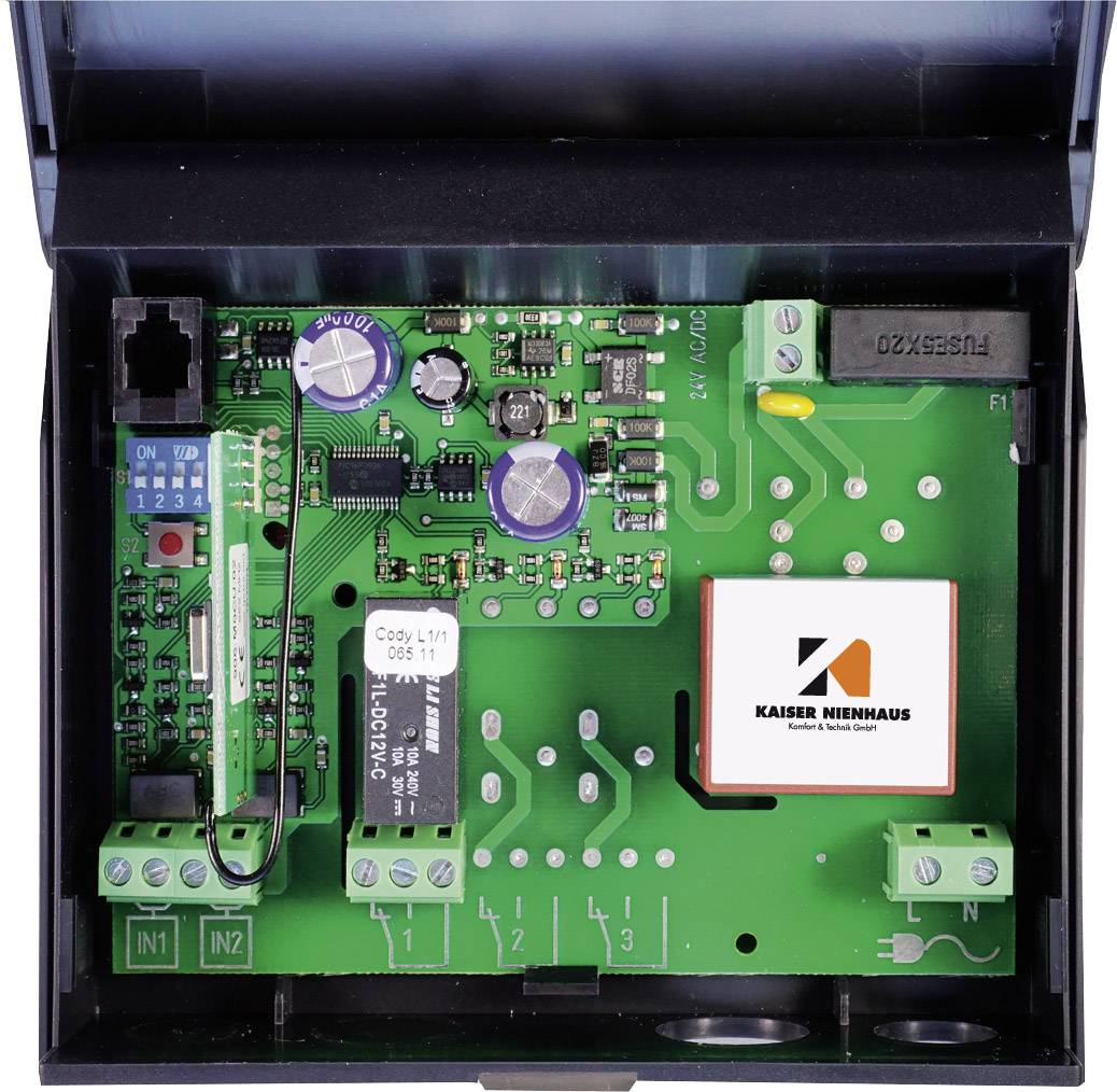 Een geopende elektronische printplaat met condensatoren, weerstanden en aansluitingen op een groene printplaatachtergrond; toont het Kaiser Nienhaus-logo.