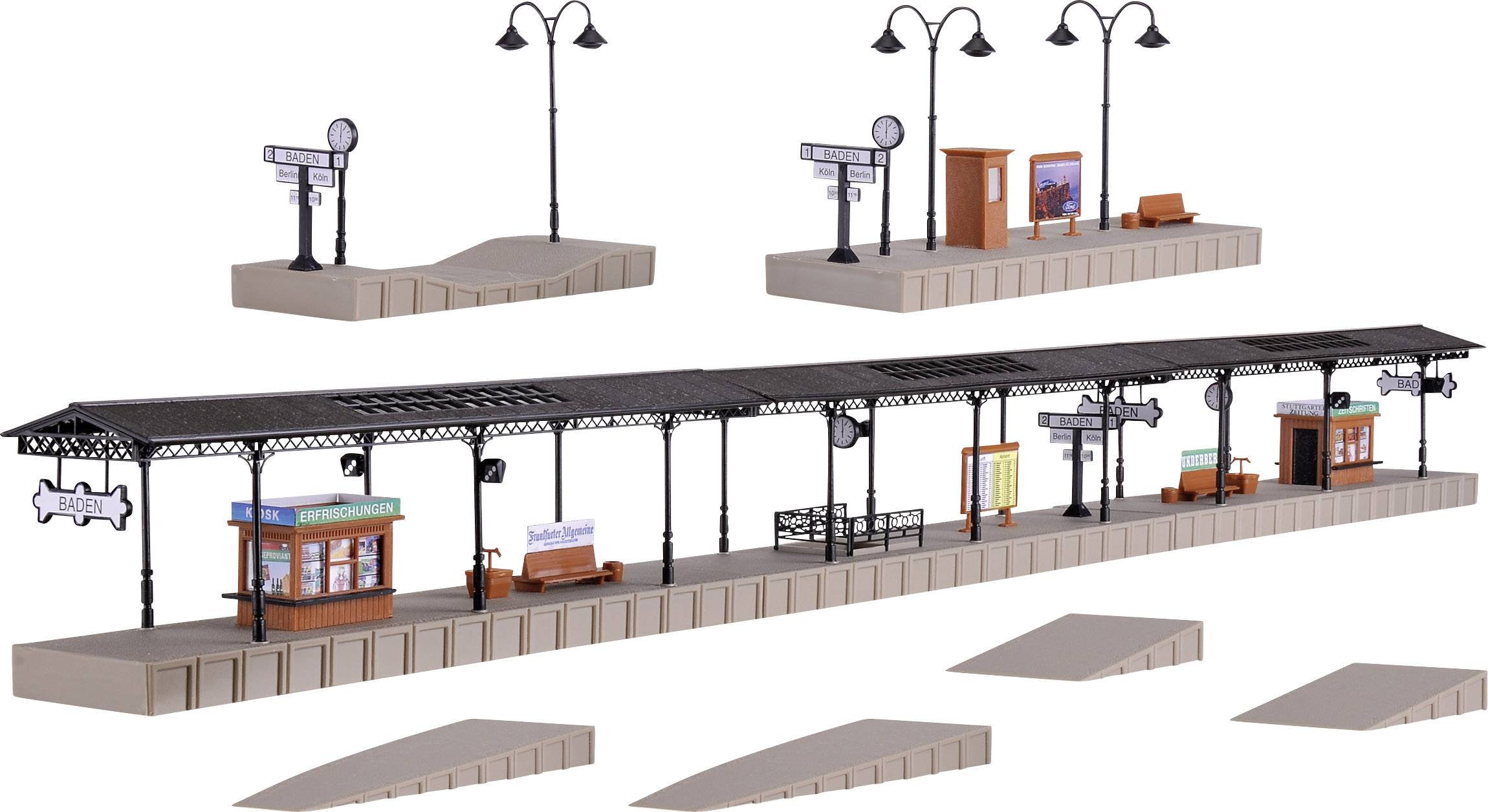 Speelgoedtreinplatform met perrons, lantaarns, zitbanken en stationsnaamborden, toont een miniatuurscène van een station.