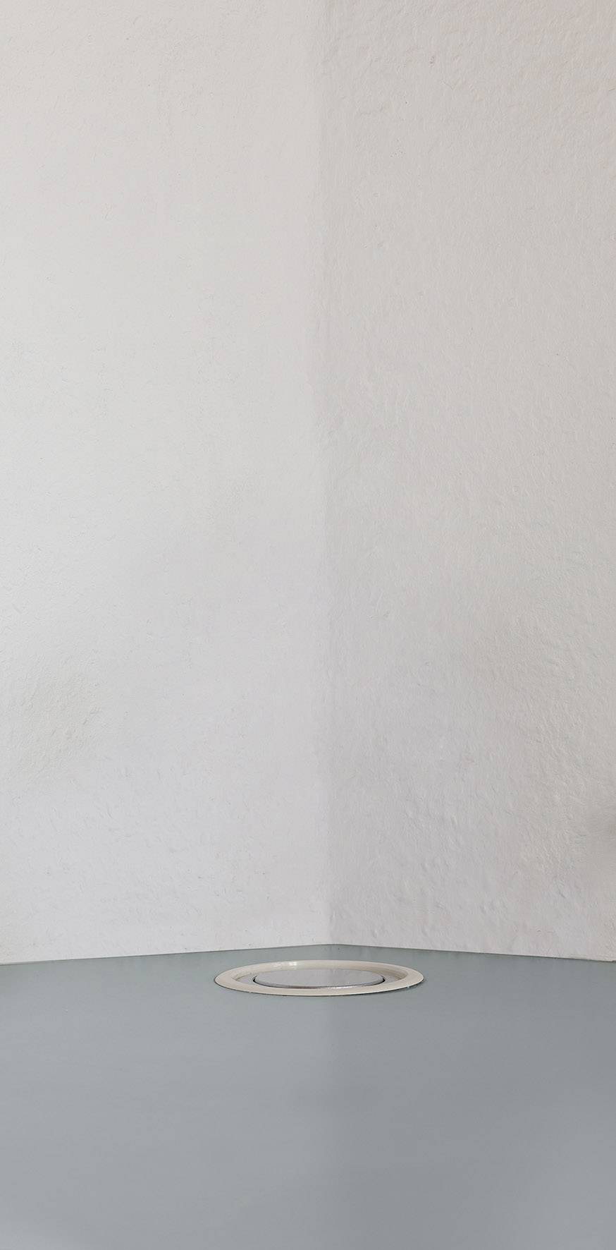 Een grijze hoek van een ruimte met een rond, zilverkleurig object op de vloer. De muren zijn wit en licht gestructureerd.