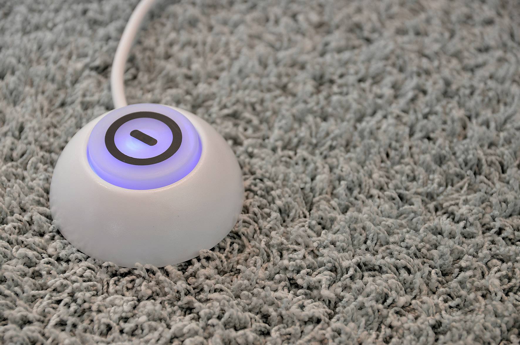 Een knop in de vorm van een ronde schakelaar met een oplichtend symbool ligt op een grijze vloerbedekking.