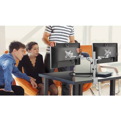 Vier personen zitten rond een tafel met twee monitors. Één persoon staat enwijst naar een scherm. Ze lijken te discussiëren.