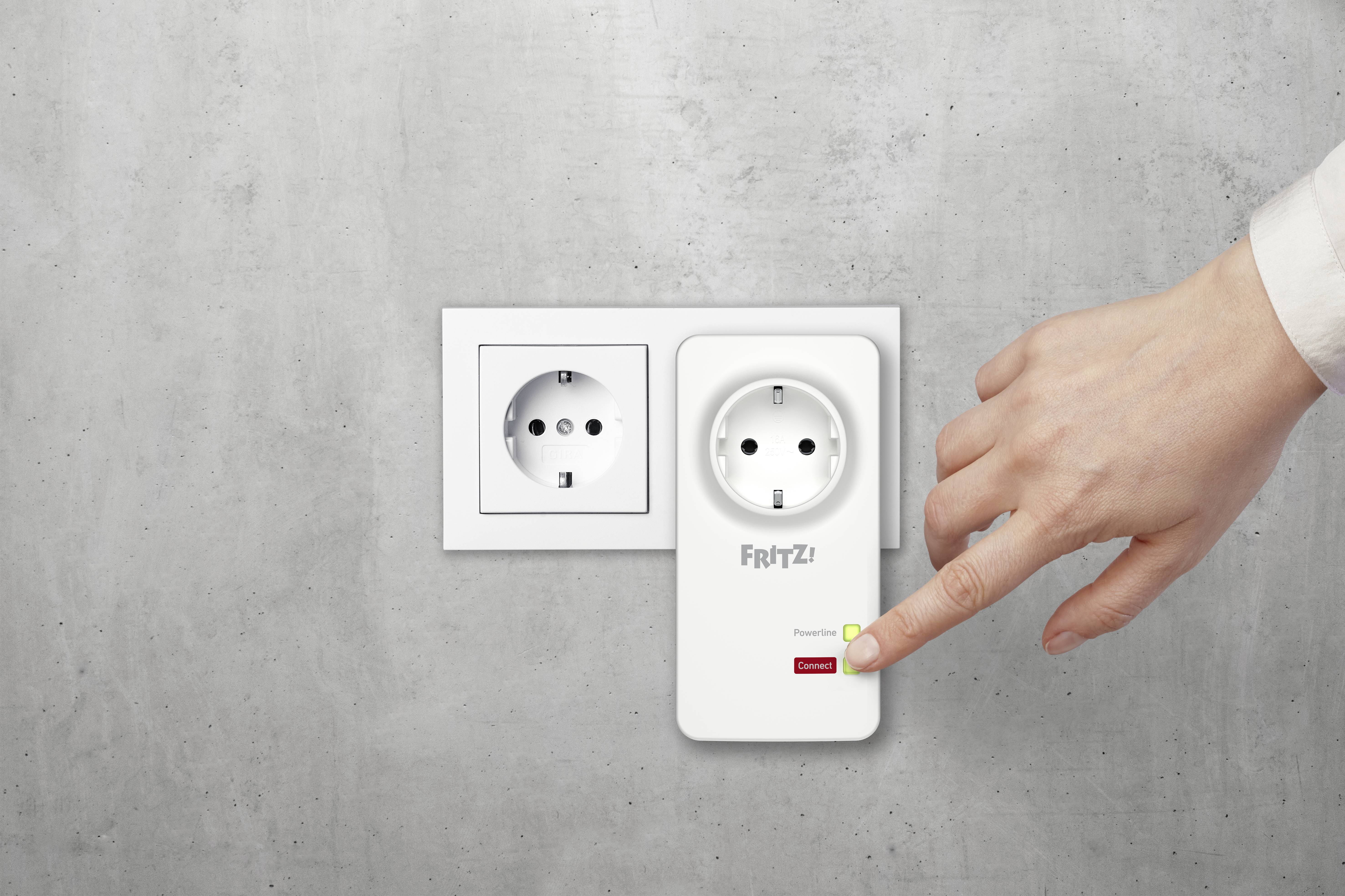 Een hand drukt op de knop van een Fritz! Powerline-apparaat dat in een stopcontact aan een betonnen muur is gestoken.