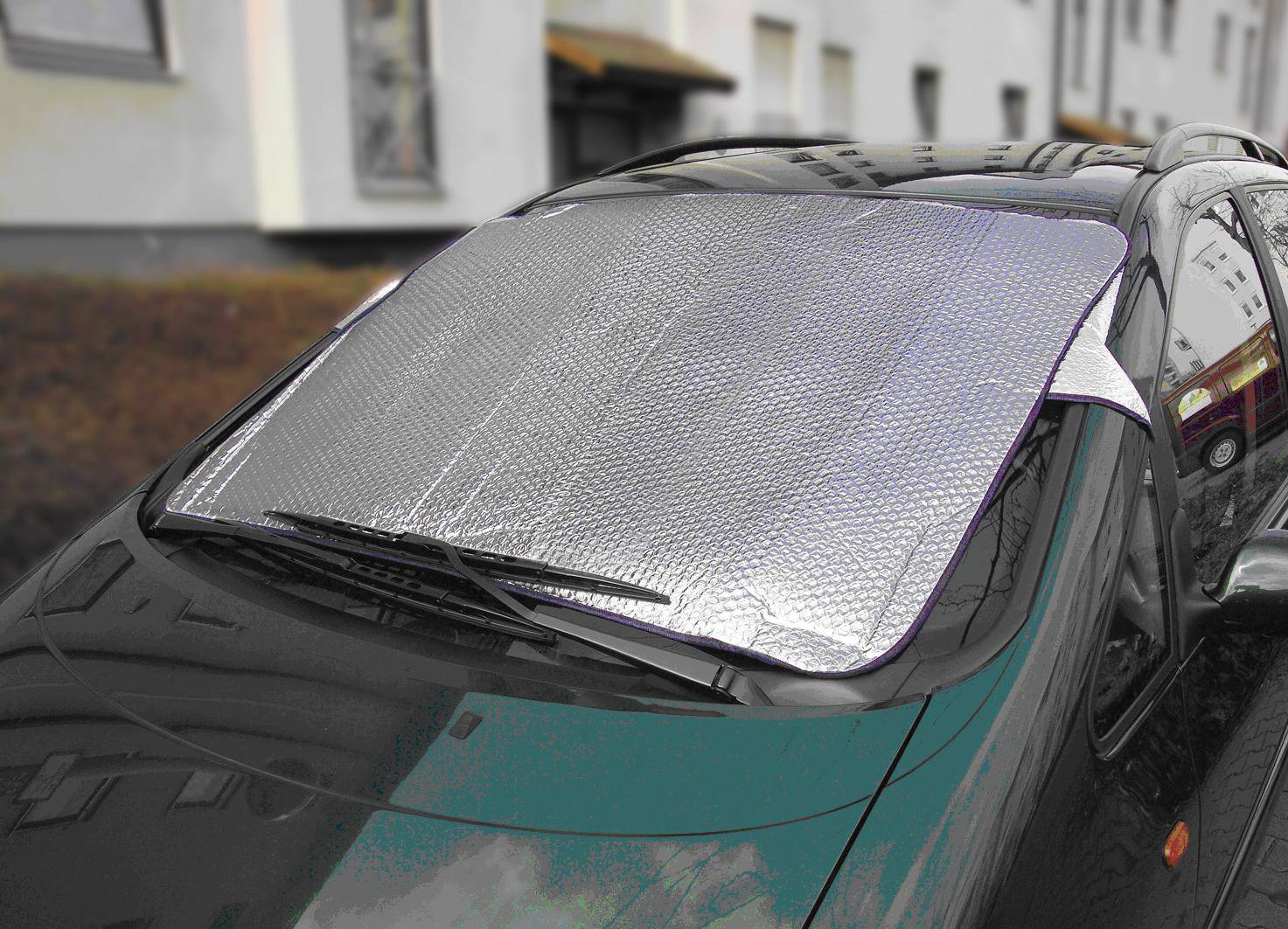 Auto met een zilveren zonnescherm op de voorruit, geparkeerd aan de straat voor een gebouw.