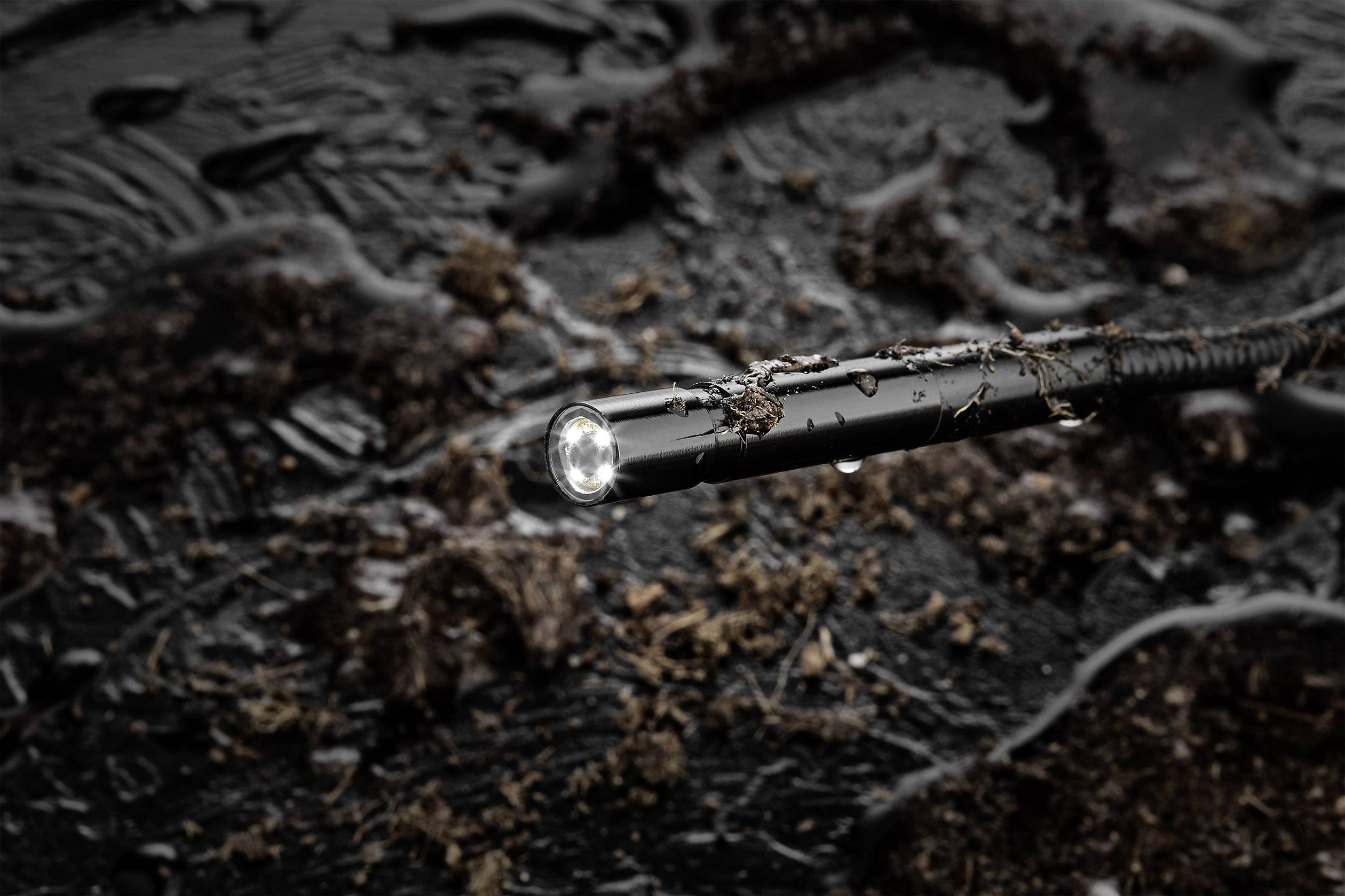 Een endoscoop-camera-kabel met een verlichte punt is ondergedompeld in vochtige, modderige grond om de omgeving te verkennen.