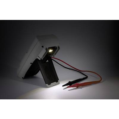 Een multimeter staat schuin op een standaard, verlicht door een kleine lamp. Een zwart en een rood snoer hangen naar beneden.