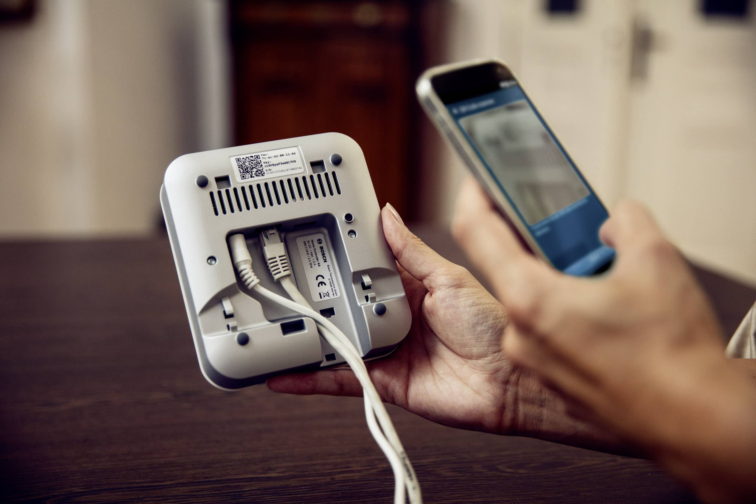 Een persoon houdt een router vast en scant de QR-code aan de achterkant met een smartphone. Er zijn twee kabels aangesloten.