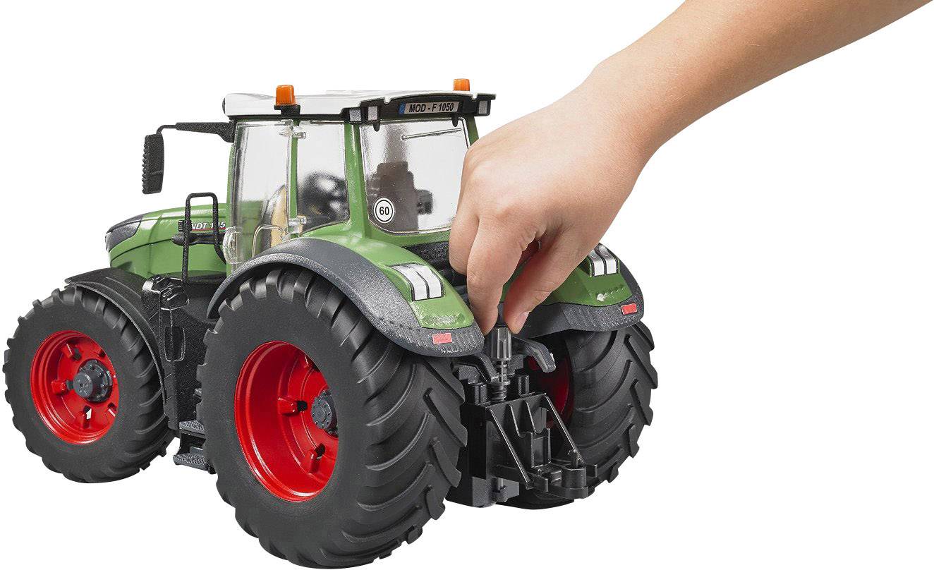 Een hand stelt een model van een groene tractor met grote zwarte banden en een rood interieur bij op een witte achtergrond.