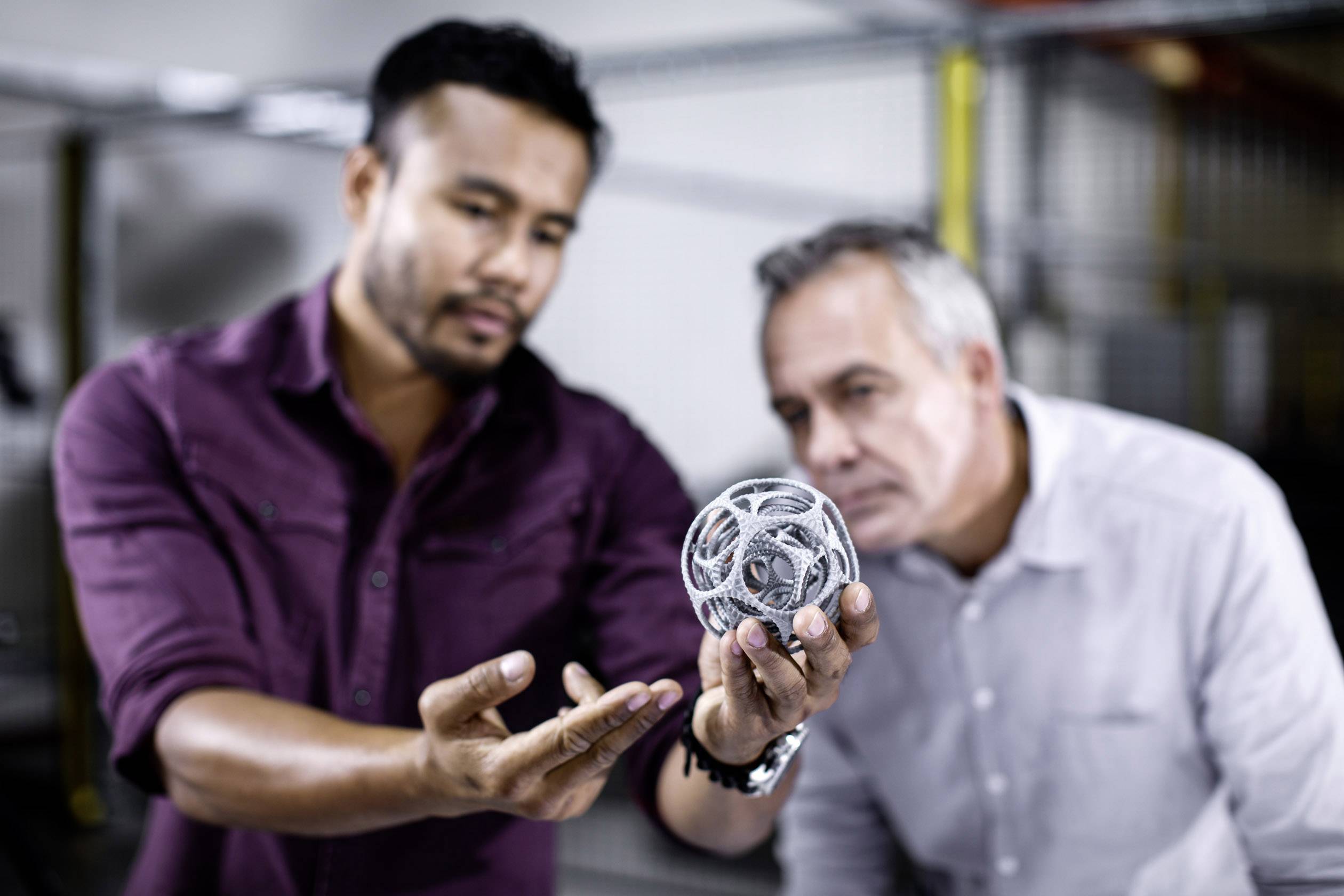 Twee mannen bekijken een complex metalen voorwerp in een laboratorium. De focus ligt op de discussie en analyse van het object.