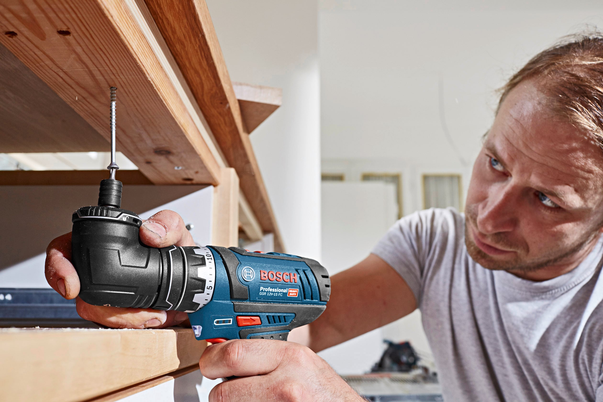 Een man gebruikt een elektrische boormachine om een plank te bevestigen. Hij is aandachtig geconcentreerd op zijn werk.