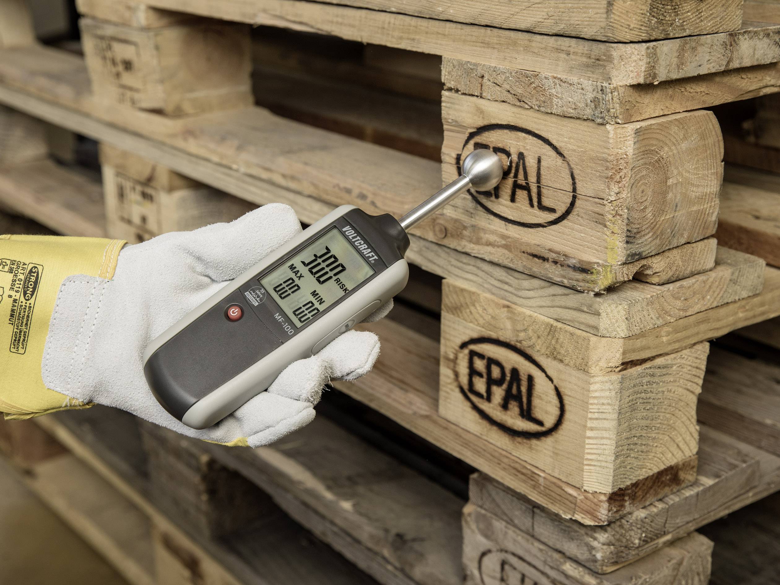 Hand met handschoen houdt een digitaal meetapparaat vast dat de vochtigheid van een EPAL-houten pallet meet. Apparaat toont 7% aan.