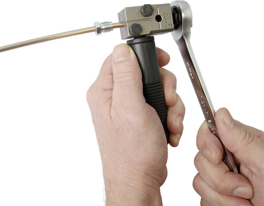 Twee handen gebruiken gereedschap om een metalen staaf te bewerken met een spaninrichting en een moersleutel.
