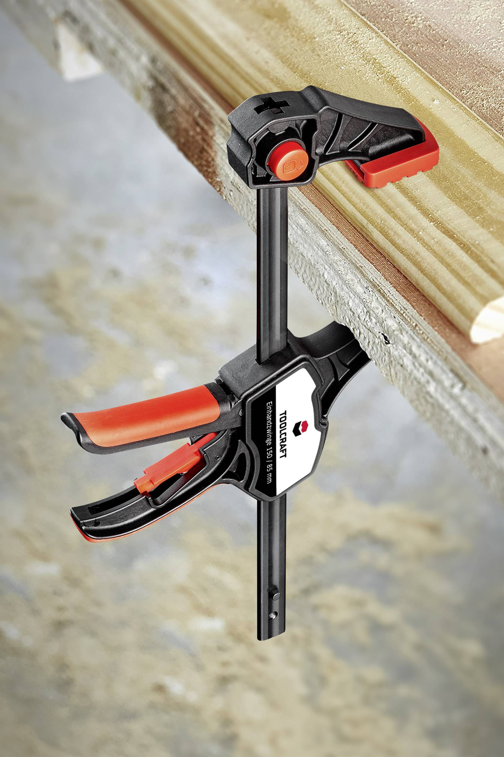 Een zwarte en rode klembeugel houdt een houten plank vast aan een tafel. Industriële achtergrond.