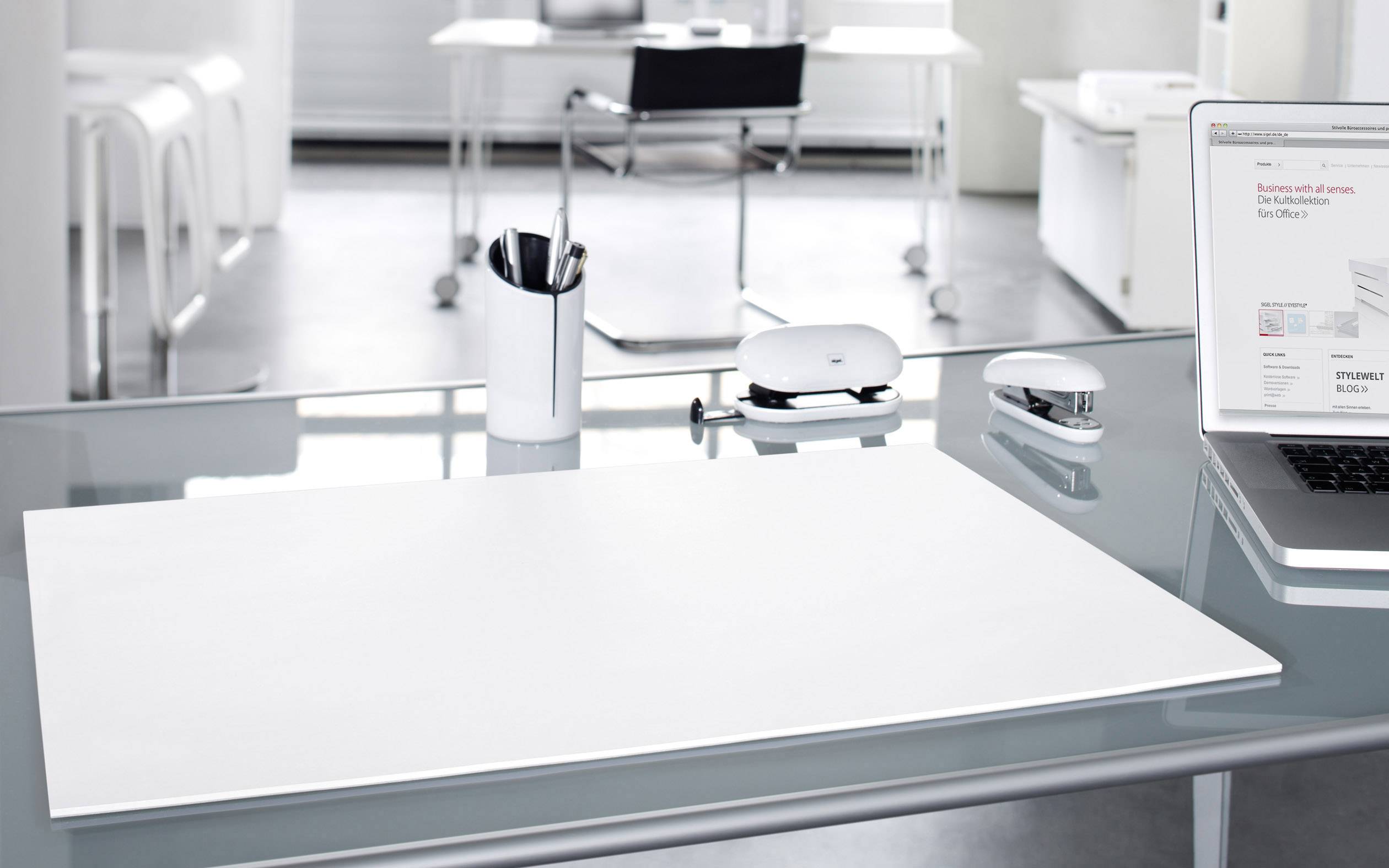 Een moderne, opgeruimde kantoorruimte met een glazen bureau, waarop kantoorbenodigdheden staan. Op de achtergrond staat een lege stoel.