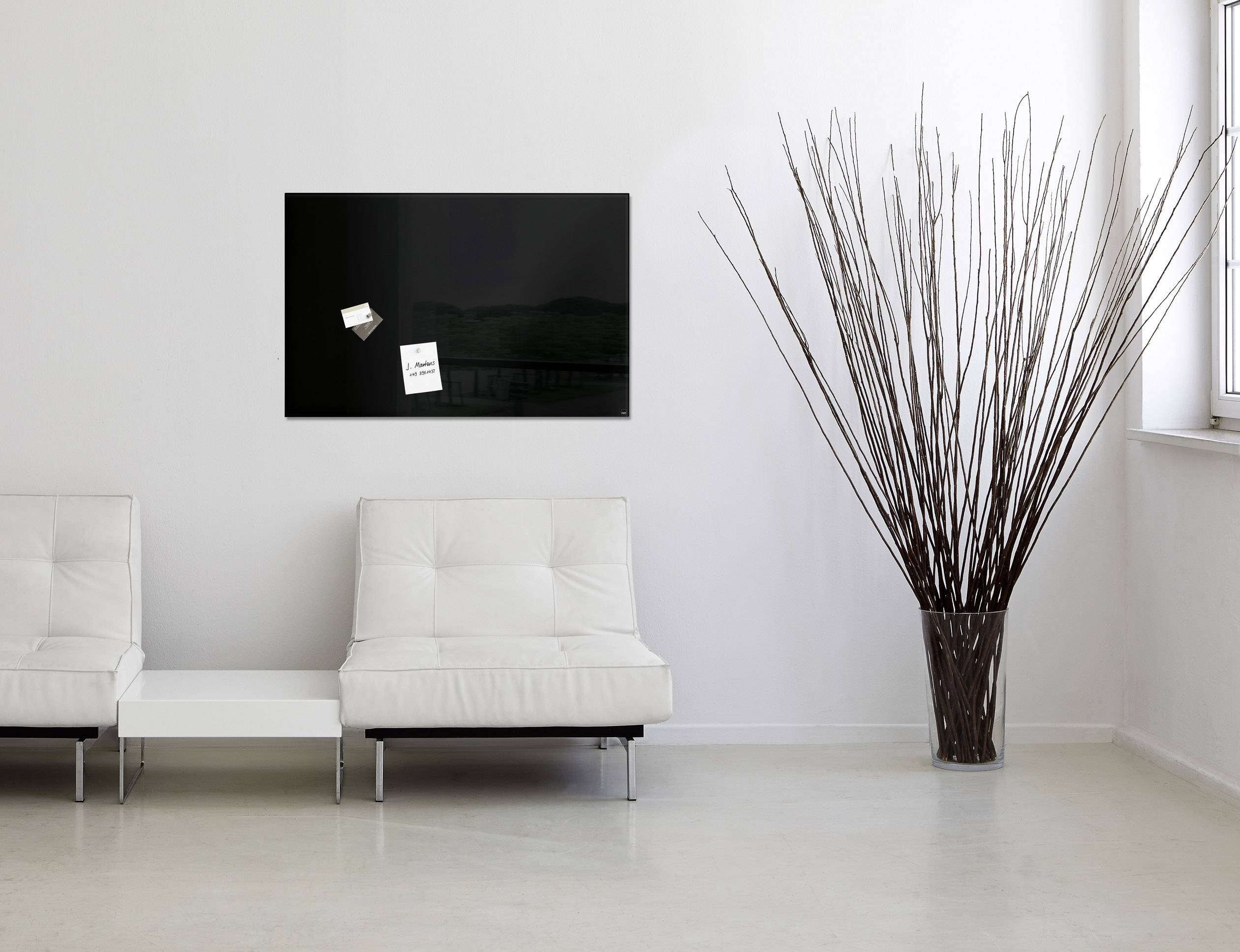 Twee witte banken in een moderne, minimalistische ruimte. Aan de muur hangt een zwart bord met kleine briefjes.