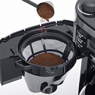 Een koffiemachine wordt gevuld met koffiemolen. Een maatlepel giet gemalen koffie in een filter in het geopende koffiecompartiment.