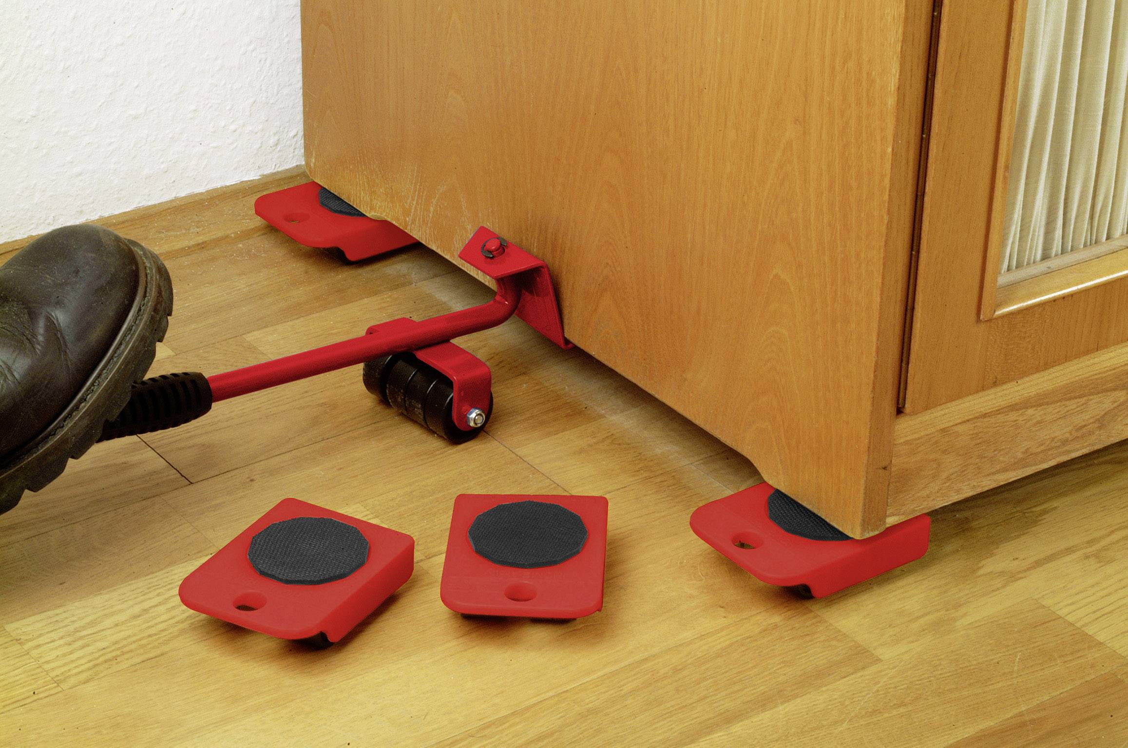 Een rood hefgereedschap wordt gebruikt om een meubelstuk op te tillen. Rode meubeldragers worden eronder geplaatst.