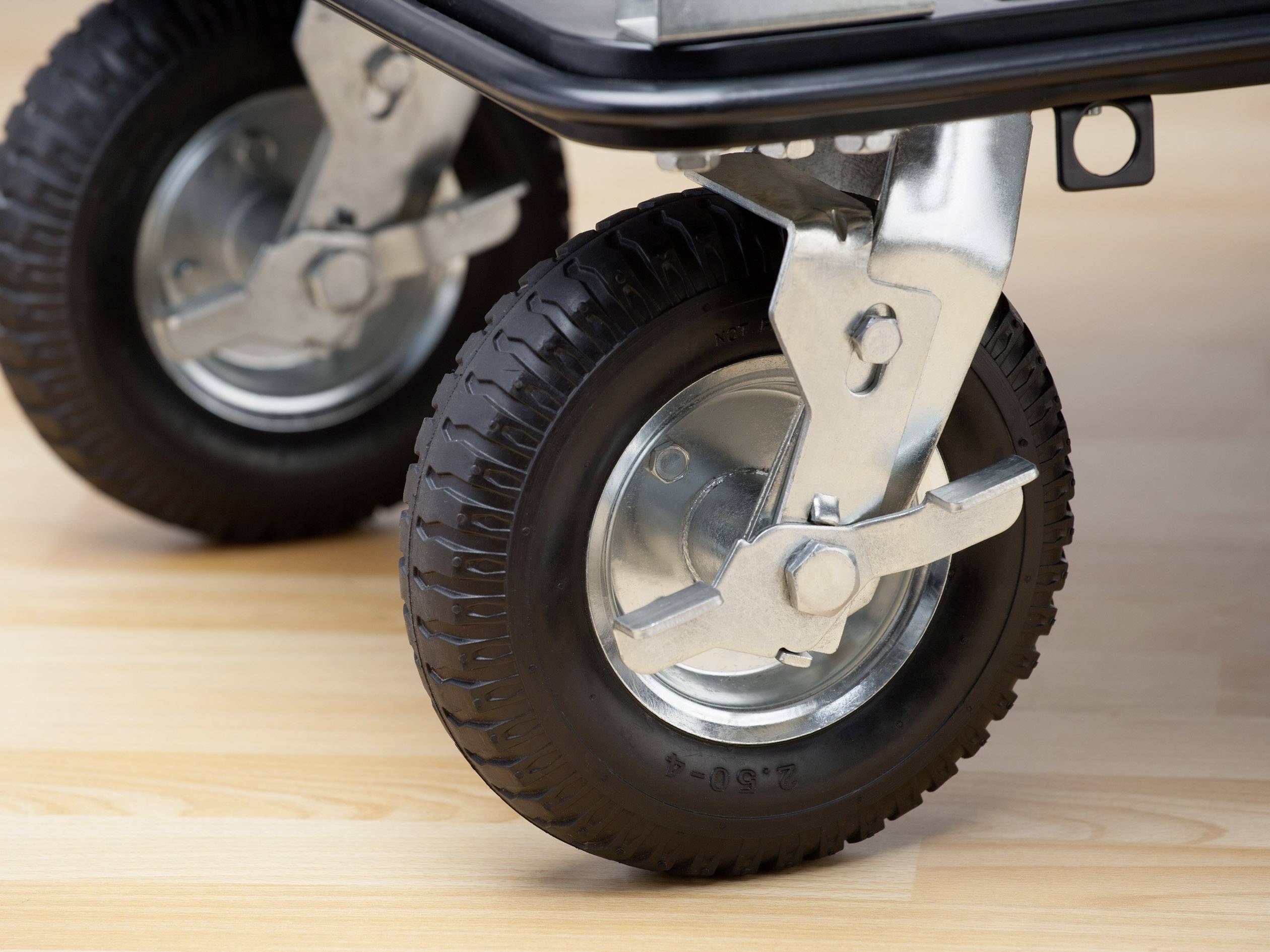 Close-up van twee stabiele, zwarte transportwielen met metalen bevestigingen op een lichte houten vloer.