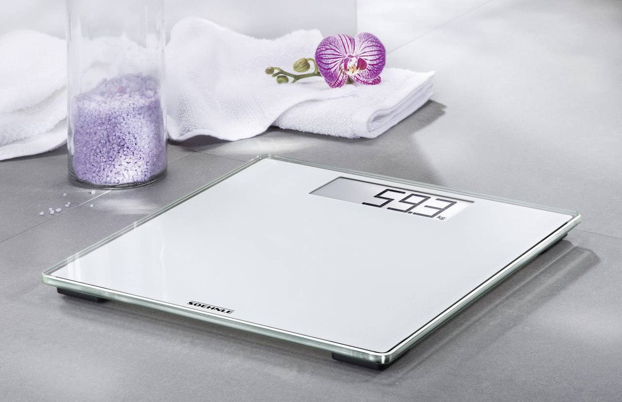 Elektronische weegschaal op de badkamervloer toont '59,3' kilogram. Ernaast liggen een handdoek en een orchideeënbloem als decoratie.