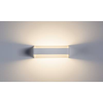 Een moderne, rechthoekige wandlamp straalt warm licht naar boven en beneden uit, creëert zachte schaduwen en zorgt voor een ontspannen sfeer.