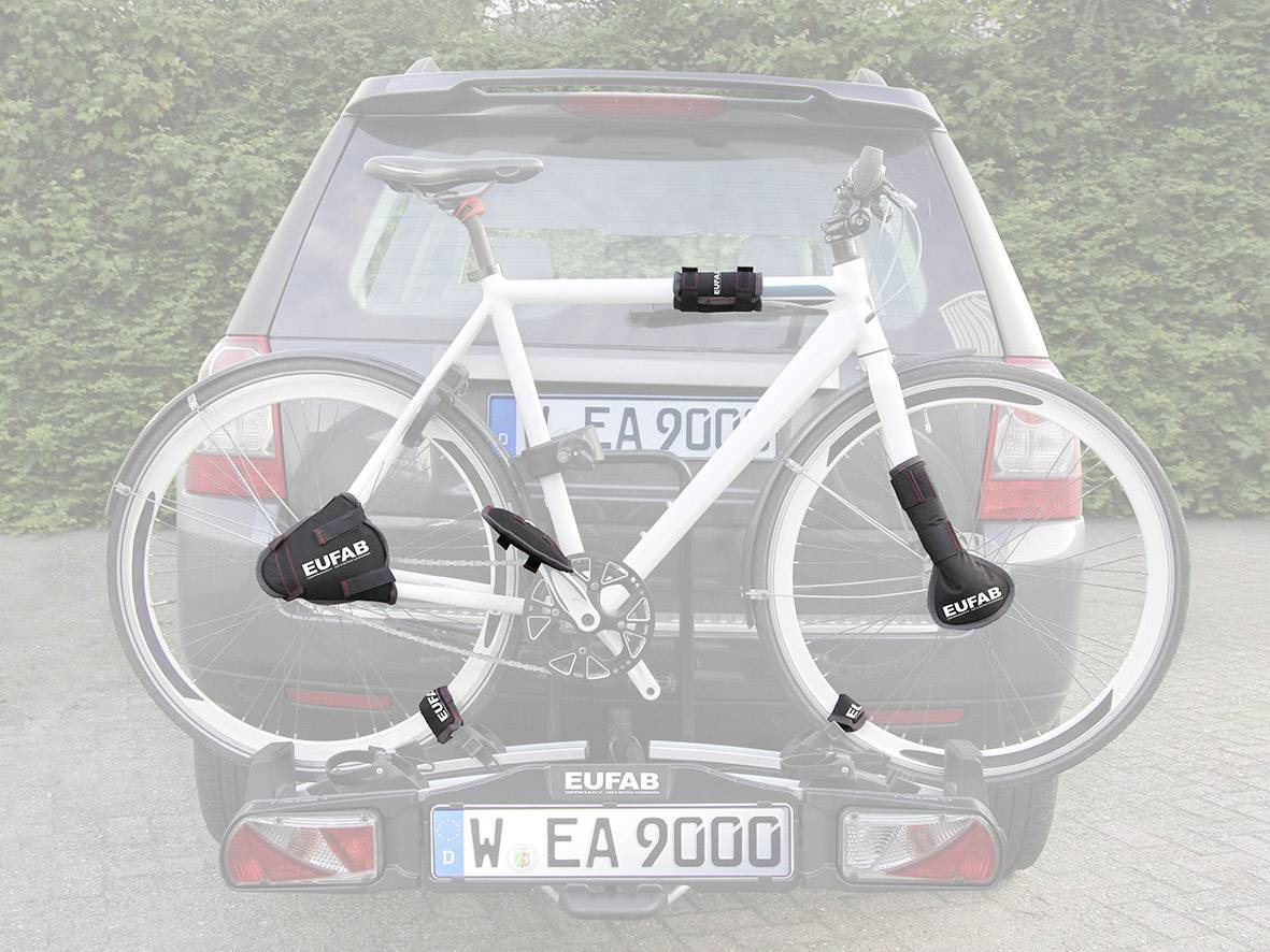 Een witte fiets is bevestigd aan een fietsendrager aan de achterkant van een zwarte auto, geparkeerd voor een haag.