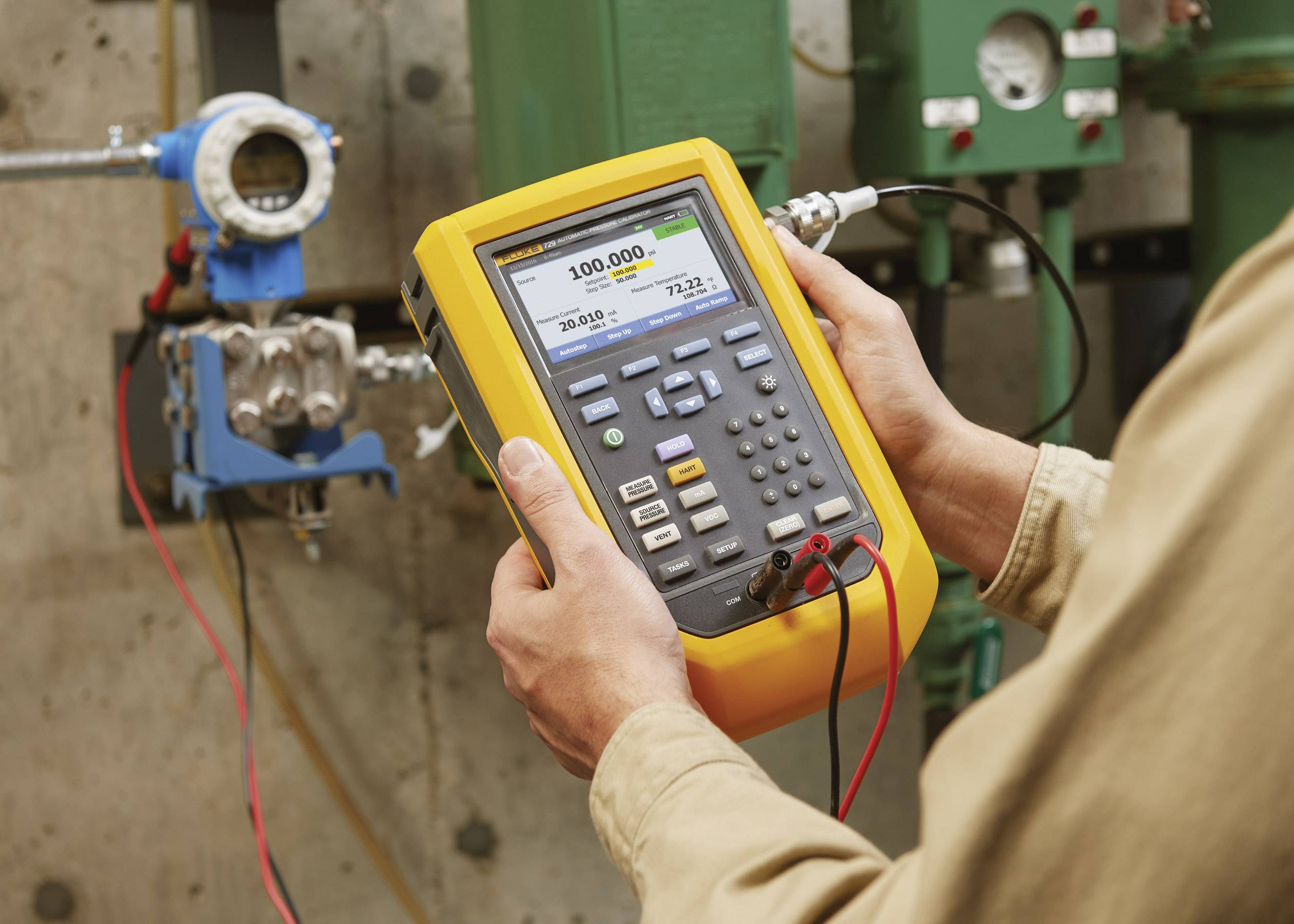 'Een persoon houdt een digitaal meetapparaat vast dat een druk van 100.000 PSI aangeeft. Achtergrond toont industriële buizen en apparatuur.'