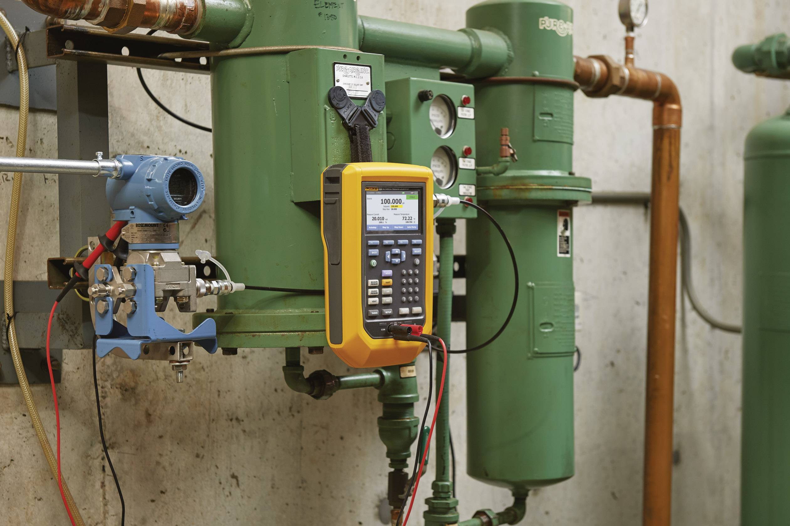 Manometer op een groen buizensysteem geeft drukwaarden weer. Ernaast zijn aansluitventielen en een geel meetinstrument voor kalibratie zichtbaar.