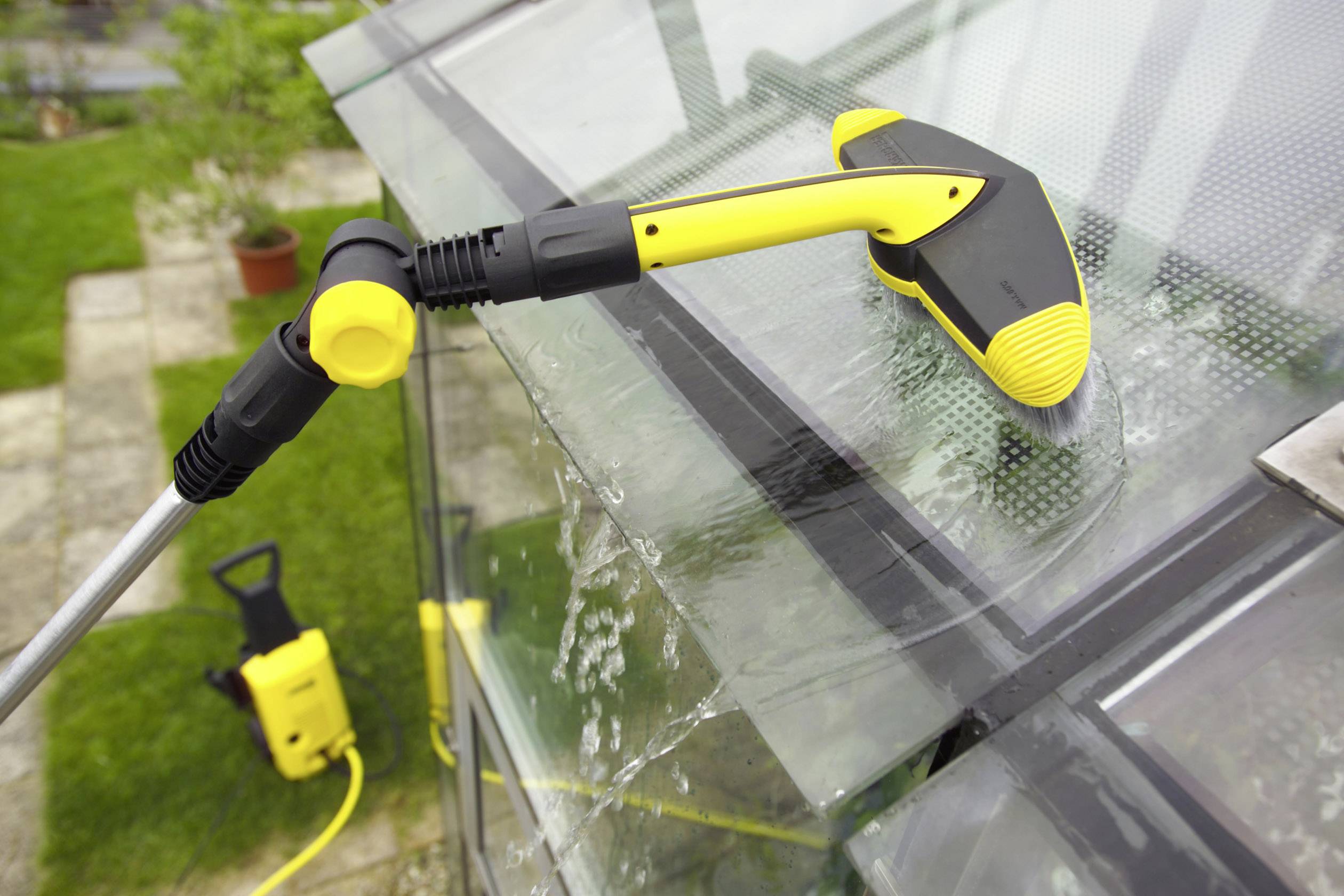 Een raamwasser reinigt met een elektrische hogedrukreiniger een glazen dak. Waterdruppels zijn zichtbaar.