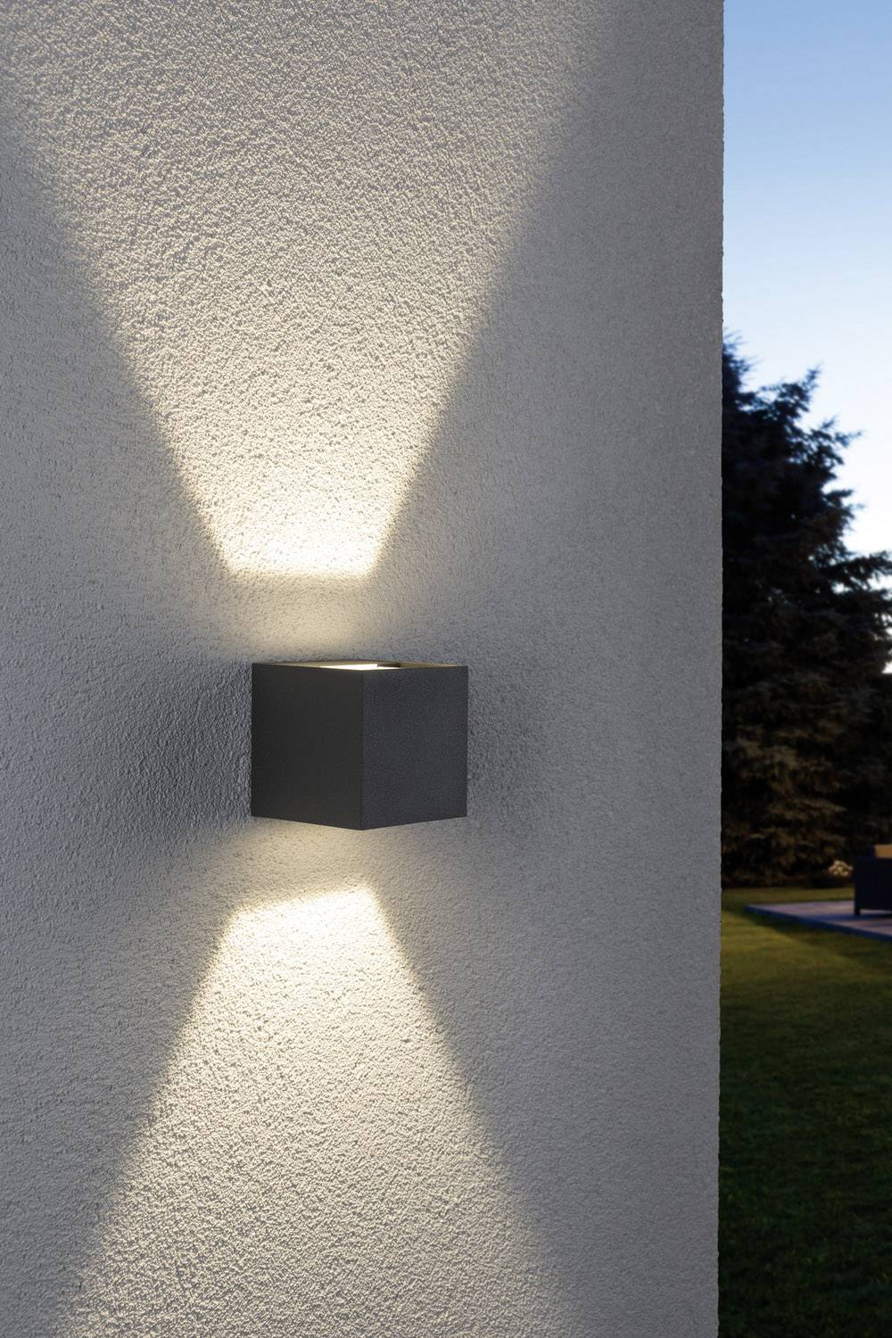 Buitenmuurlamp straalt naar boven en beneden, creëert een stijlvol lichtpatroon op de betonnen muur bij het invallen van de schemering.