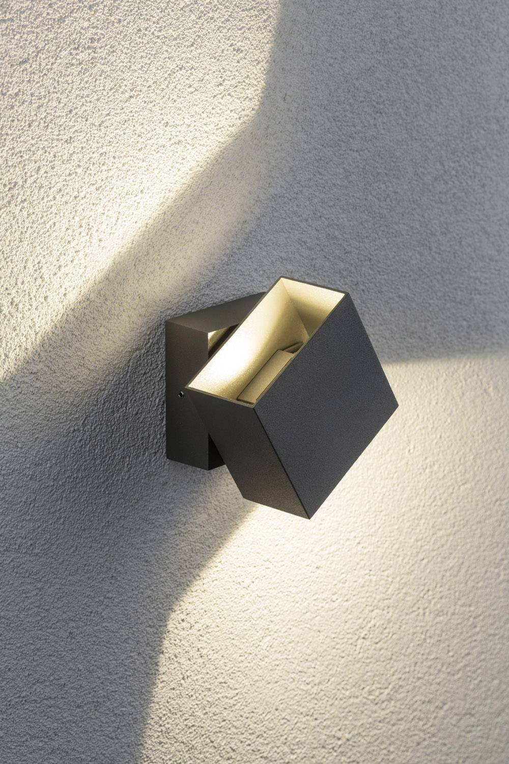 Zwarte, vierkante wandlamp die warmwit licht verspreidt naar boven en beneden op de beige muur, modern design.