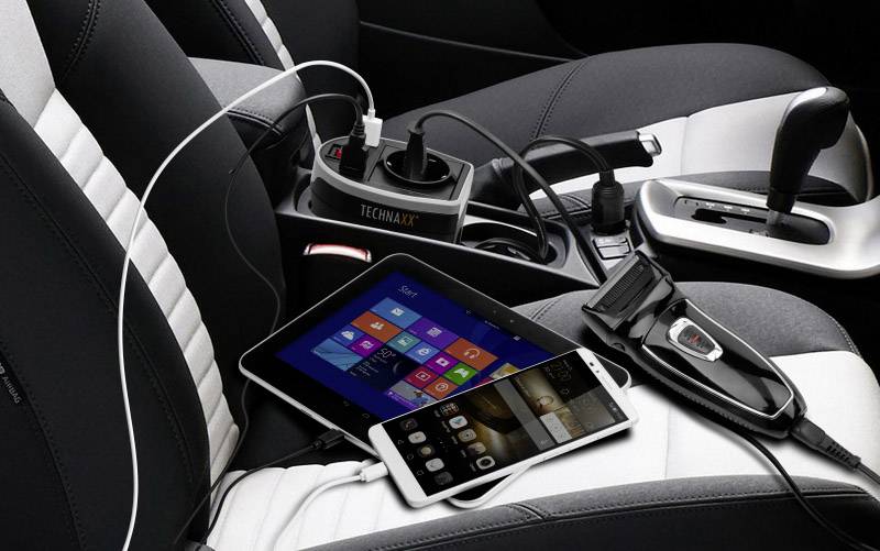 Een auto-interieur met een aangesloten stekkerdoos. Tablet en smartphone worden tegelijkertijd opgeladen, een scheerapparaat is aangesloten.