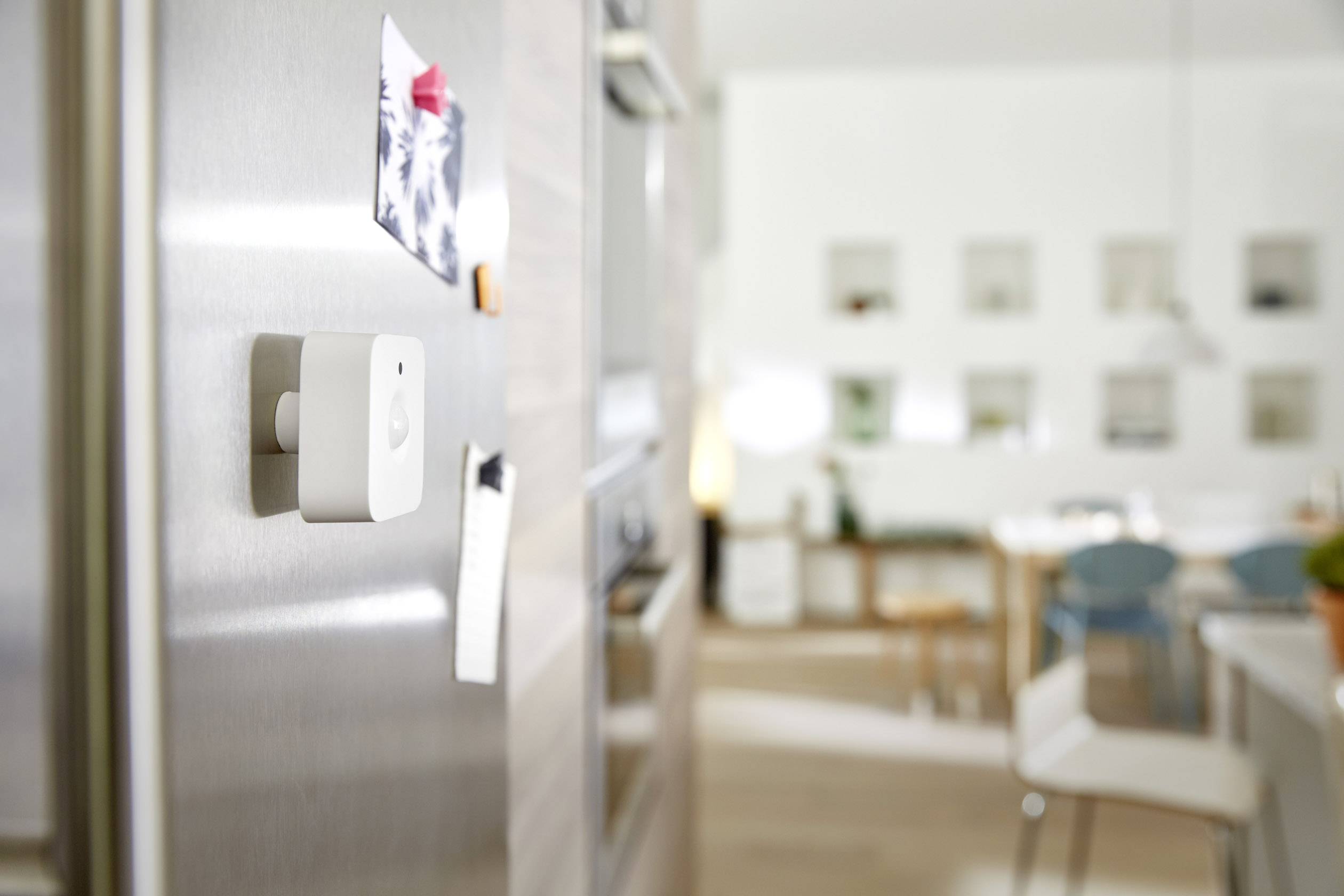 Een vierkante sensor aan de deur van een koelkast in een moderne keuken, toont slimme technologie in een alledaagse omgeving.