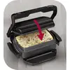 Een contactgrill met een pijl toont hoe het deksel wordt gesloten op een pizza met kaas en groenten.
